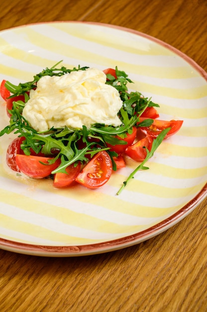 Frühlingsgemüsesalat mit Tomaten auf weißem Teller auf hölzernem Hintergrund