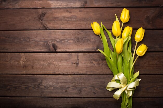 Frühlingskarte: gelbe Tulpen auf einem dunklen hölzernen Hintergrund. Draufsicht, flach liegen.