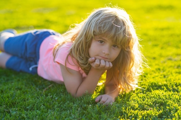 Frühlingskindgesicht Lächelnder Kindjunge mit Grashintergrund Glückliches Kind, das auf grünem Gras liegt Lächelnder Junge, der Spaß im Freien im Garten hat