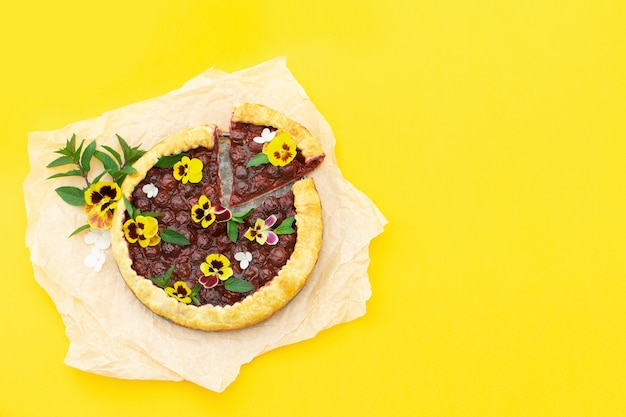 Frühlingskirschkuchen, verziert mit essbaren Blumen auf einem Gelb.