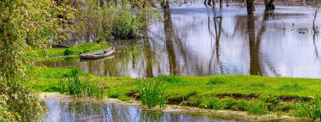 Frühlingslandschaft mit einem Boot am Fluss und der Reflexion von Bäumen im Wasser