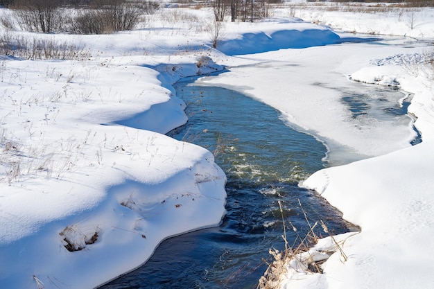 Frühlingslandschaft mit einem unter Eis liegenden Fluss und Schneestürmen am Ufer März