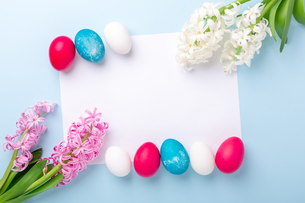 Frühlingsmodell mit Ostereiern, Hyazinthen und Rohling des weißen Papiers auf blauem Hintergrund. Osterkonzept. Speicherplatz kopieren. Draufsicht - Bild