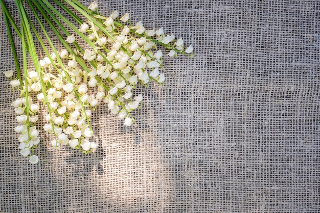 Frühlingsstrauß der weißen Maiglöckchen auf einem Hintergrund der Sackleinen, Leinwandstoff im Sonnenlicht, Draufsicht, Kopienraum