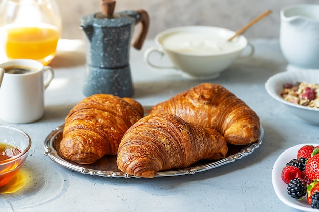 Frühstück am Morgen mit frisch gebackenen Croissants, Beeren, Müsli, Kaffee, Milch, Joghurt, Honig, Saft