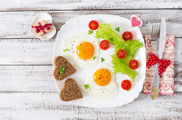 Frühstück am Valentinstag - Spiegeleier und Brot in Form eines Herzens und frischen Gemüses. Ansicht von oben