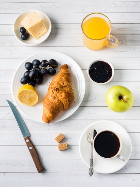 Frühstück auf einem weißen Tabellen-Kaffee-Hörnchenorangensaft Trauben-Apple-Schokolade