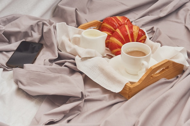 Frühstück auf einem zerknitterten Bett, Kaffee, Croissants, Handy