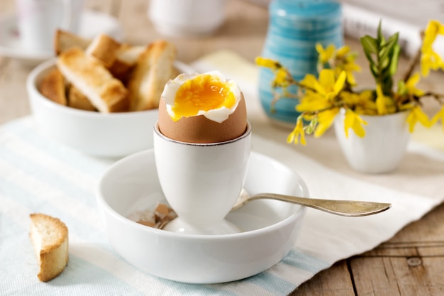 Frühstück aus weichgekochtem Ei, Toastbrot, Kaffee mit Sahne und frischer Zeitung.