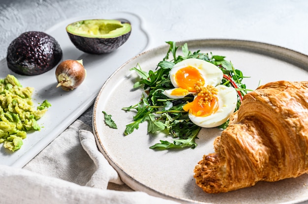 Frühstück, Brunch mit Avacado, Rucola, Croissant und Ei. Grauer Hintergrund. Draufsicht