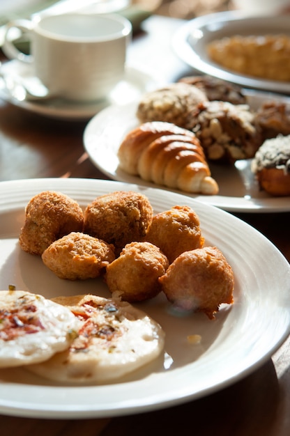 Frühstück, das aus Hörnchen-, Brötchen-, Bonbon-, Donut- und Bananenbällen auf weißen Platten besteht