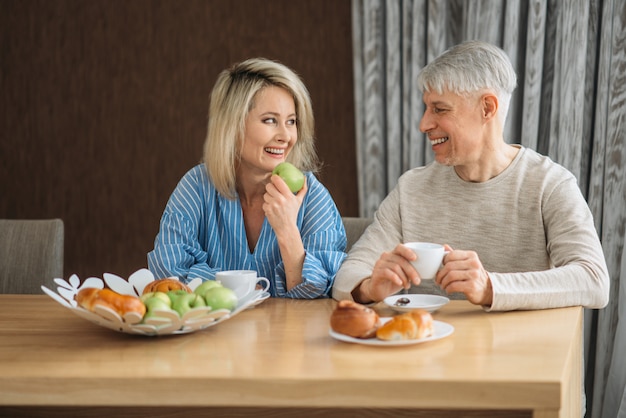 Frühstück des erwachsenen Liebespaares zu Hause. Reifer Ehemann und Ehefrau sitzen in der Küche, glückliche Familie, Mann und Frau trinken Kaffee am Tisch mit Früchten