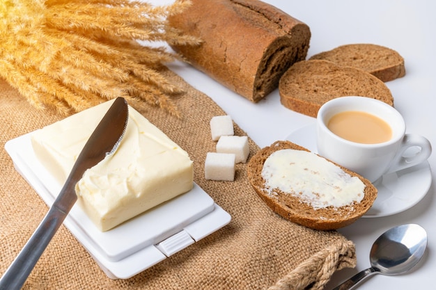 Frühstück, eine Tasse Kaffee, Butter in einer Butterdose und Roggenbrot auf Sackleinen