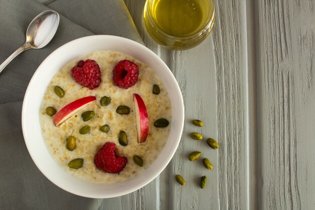 Frühstück: Haferflocken mit Apfel, Himbeeren, Honig und Nüssen auf dem grauen hölzernen Hintergrund. Draufsicht.