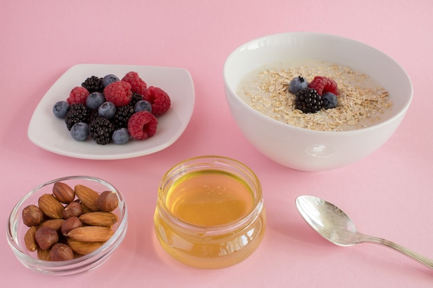 Frühstück: Haferflocken mit Beeren, Honig und Nüssen auf dem rosa Hintergrund