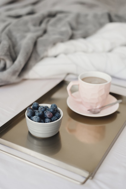 Frühstück im Bett: frische Blaubeeren und Kaffee mit Milch in einer rosa Tasse