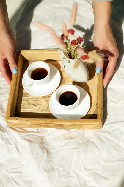 Frühstück im Bett, weibliche Hände versuchen mit zwei Tassen Kaffee und Blume im Sonnenlicht zu Hause, Zimmermädchen bringt Tablett mit Frühstück im Hotelzimmer, guter Service?