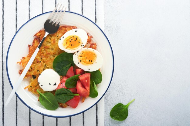 Frühstück Kartoffeln Latkes mit Sauerrahm-Spinat-Salat-Tomaten und gekochten Eiern auf hellem Hintergrund Leckeres Essen zum Frühstück Draufsicht