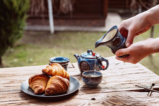 Frühstück mit chinesischem Tee und frischem Gebäck, aromatische Buttercroissants. Frauenhände gießen Tee. Tee-Zeremonie.