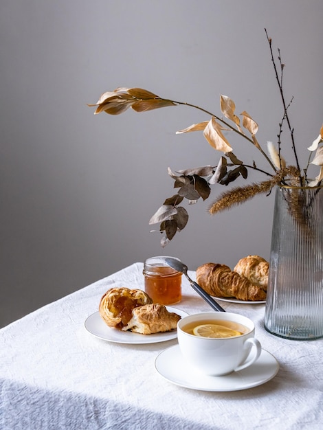 Frühstück mit Croissant und schwarzem Tee mit Zitrone Hausgemachtes Frühstück für eine Person