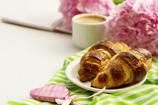 Frühstück mit Croissants, rosa Rosenblüte und Kaffee