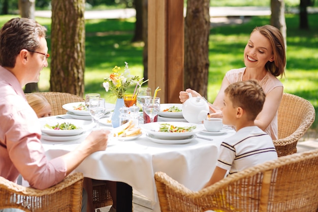 Frühstück mit den Eltern. Kleiner blonder Sohn, der mit den Eltern frühstückt, während er vor ihrem Einfamilienhaus sitzt