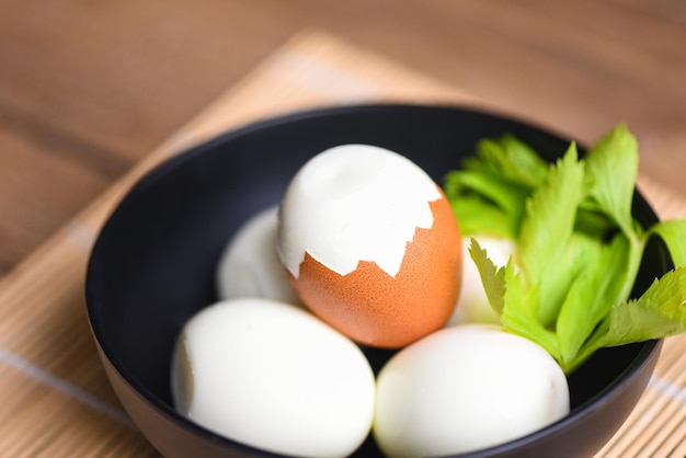 Frühstück mit Eiern, Menü mit frischen geschälten Eiern, gekochte Eier in einer Schüssel, die mit Blättern grüner Sellerie auf Holzhintergrund dekoriert ist, Konzept für gesunde Ernährung mit Eiern