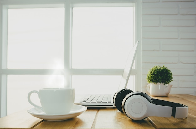 Frühstück mit einer Tasse warmen Kaffees auf dem Tisch im Büro mit Laptop.