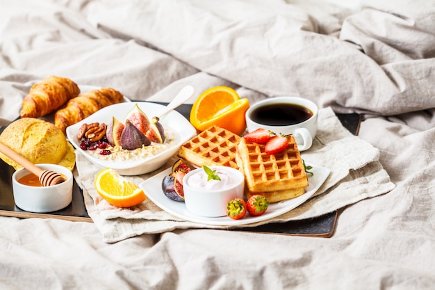 Frühstück mit Haferflocken, Waffeln, Kaffee, Croissants und Früchten im Bett,