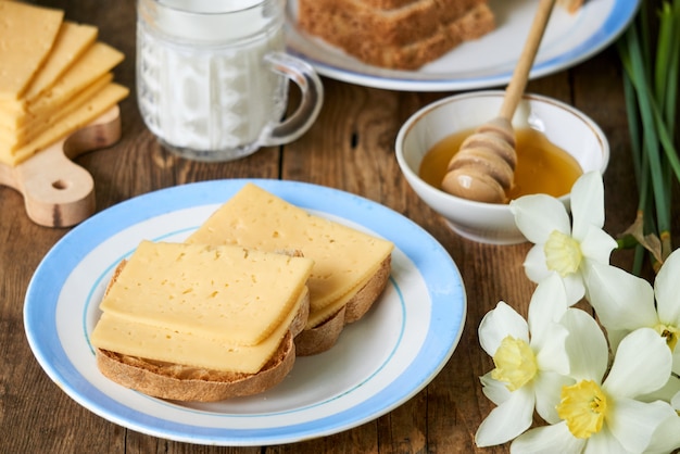 Frühstück mit Käsesandwich, Milch und Honig auf einem Holztisch