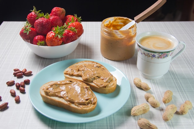 Frühstück mit Kaffee und Sandwiches mit Erdnusspaste und Erdbeeren