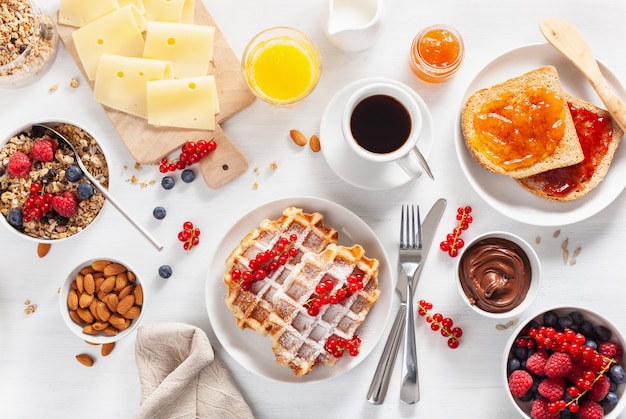 Frühstück mit Müsli-Beeren-Nüssen, Waffel, Toast, Marmelade, Schokoladenaufstrich und Kaffee. Draufsicht