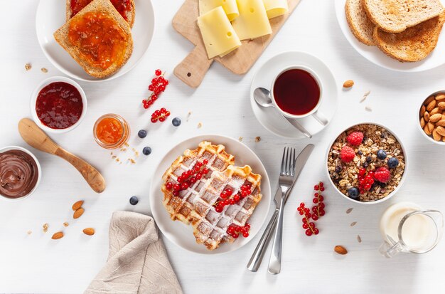 Frühstück mit Müsli-Beeren-Nüssen, Waffel, Toast, Marmelade, Schokoladenaufstrich und Kaffee. Draufsicht