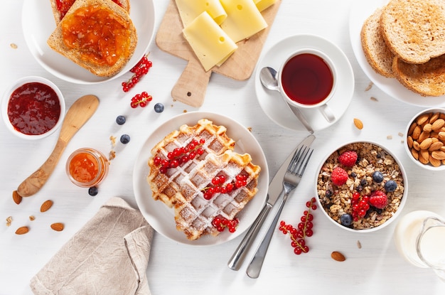 Frühstück mit Müsli-Beeren-Nüssen, Waffel, Toast, Marmelade, Schokoladenaufstrich und Kaffee. Draufsicht