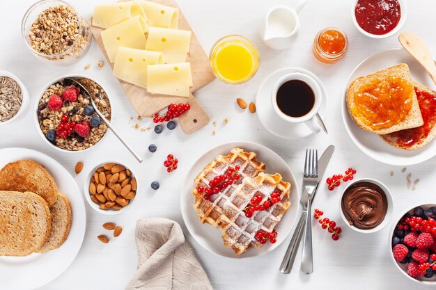 Frühstück mit Müsli-Beeren-Nüssen, Waffel, Toast, Marmelade, Schokoladenaufstrich und Kaffee. Draufsicht