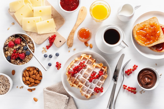 Frühstück mit Müsli-Beeren-Nüssen, Waffel, Toast, Marmelade, Schokoladenaufstrich und Kaffee. Draufsicht