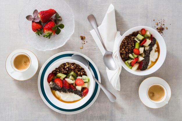 Frühstück mit Müslijoghurt, frischem Obst, Chiasamen, Ahornsirup und Beeren in Tellern auf dem Tisch