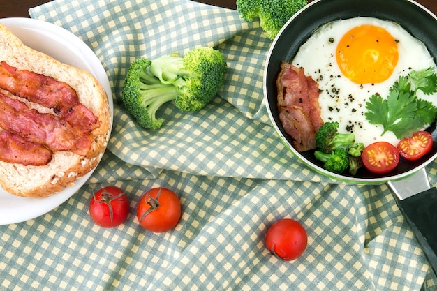 Frühstück mit Spiegelei und Speck in der dunklen Wanne auf dem Tisch