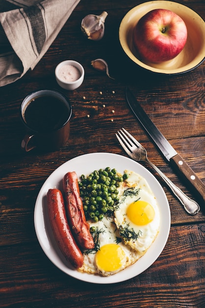 Frühstück mit Spiegeleierwürsten und Erbsen auf weißem Teller