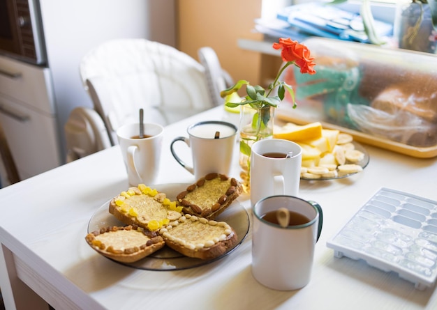 Frühstück mit Tee und Kaffee, Obststückchen, Toast mit Butter und Nüssen auf dem Tisch in der Küche morgens