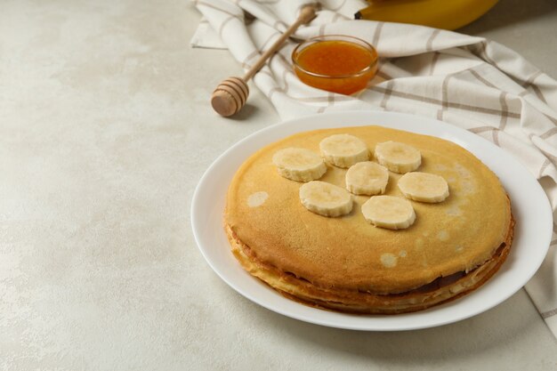 Frühstück mit Teller mit dünnen Pfannkuchen mit Banane und Marmelade auf weißer strukturierter Oberfläche