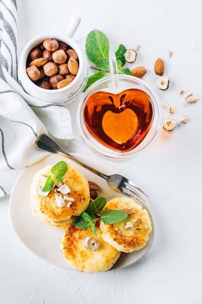 Frühstück oder Mittagessen Konzept. Hüttenkäsepfannkuchen mit Honig, Nüssen und Minze auf weißem Hintergrund