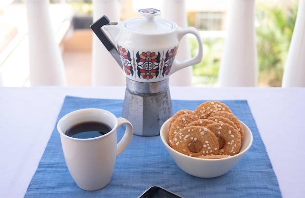 Frühstück oder Pause im Freien auf dem Balkon mit Kaffeetasse und hausgemachten Keksen Handy in der Ecke Vintage-Keramik-Kaffeemaschine