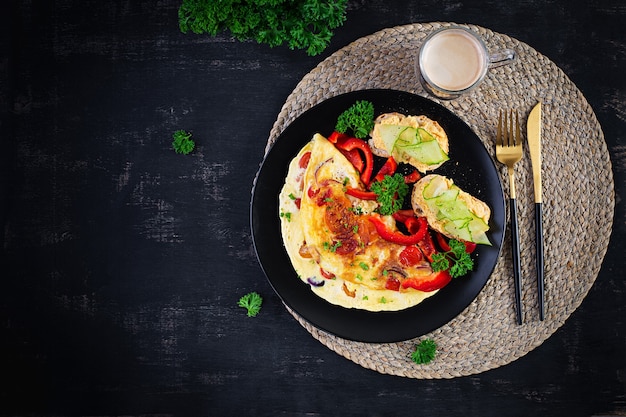 Frühstück. Omelett mit Paprika, Käse und Tomaten mit Sandwiches auf schwarzem Teller. Frittata - italienisches Omelett. Ansicht von oben, oben