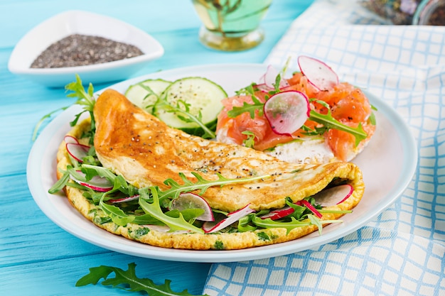 Frühstück. Omelett mit Rettich, grünem Arugula und Sandwich mit Lachsen auf weißer Platte