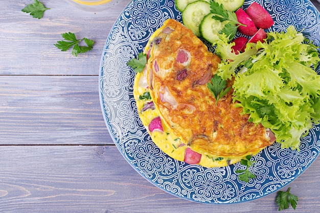 Frühstück. Omelett mit Rettich, roter Zwiebel und frischem Salat auf blauer Platte. Frittata - italienisches Omelett. Ansicht von oben