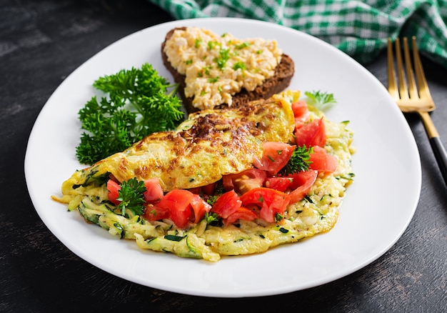 Frühstück. Omelett mit Zucchini-, Käse- und Tomatensalat mit Sandwich auf weißem Teller. Frittata - italienisches Omelett.