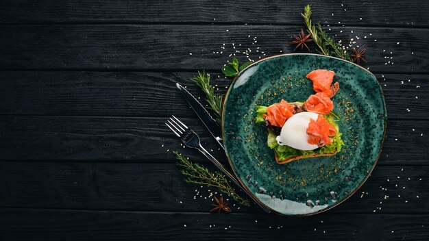 Frühstück Pochierter Eierlachs auf Salat auf Toastbrot auf schwarzem Holzhintergrund Kopierbereich