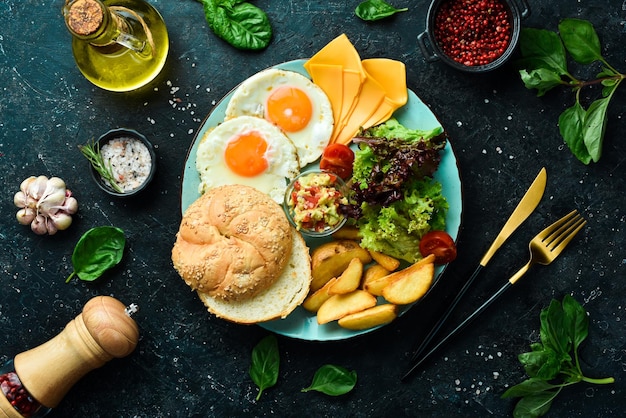Frühstück Rührei-Brötchen-Käse-Salat und Soße auf schwarzem Steinhintergrund