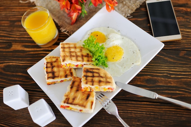 Frühstück - Sandwiches mit Mais auf einem hölzernen Hintergrund auf einem Hintergrund von Rührei, Sackleinen, Smartphone und Blumen